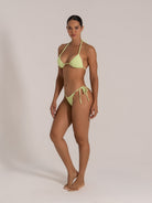 Angled pose of model in lime green tie-side bikini with textured finish and flattering silhouette.