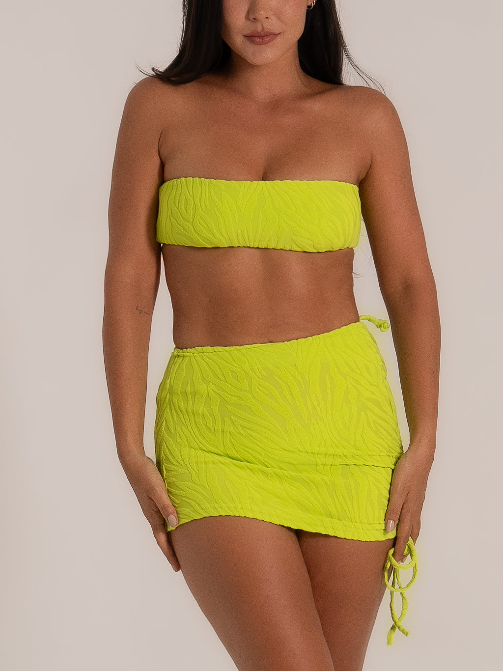 Model wears lime green textured bikini bottom with matching ruched mini skirt cover, bandeau bikini top.
