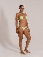 Model posing in a textured lime green bikini set, showcasing side angle with adjustable tie sides.