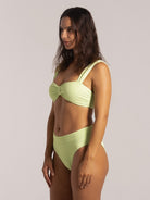 Model turning in a lime green bikini top featuring wide straps and textured material