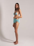 Woman modeling mint blue side-tie bikini cover-up skirt in textured fabric, side angle