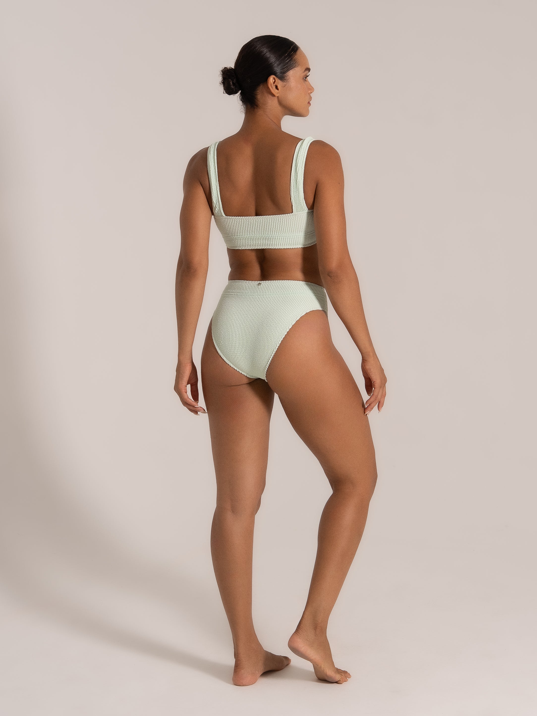 Back angled view of model showcasing mint green textured bikini set