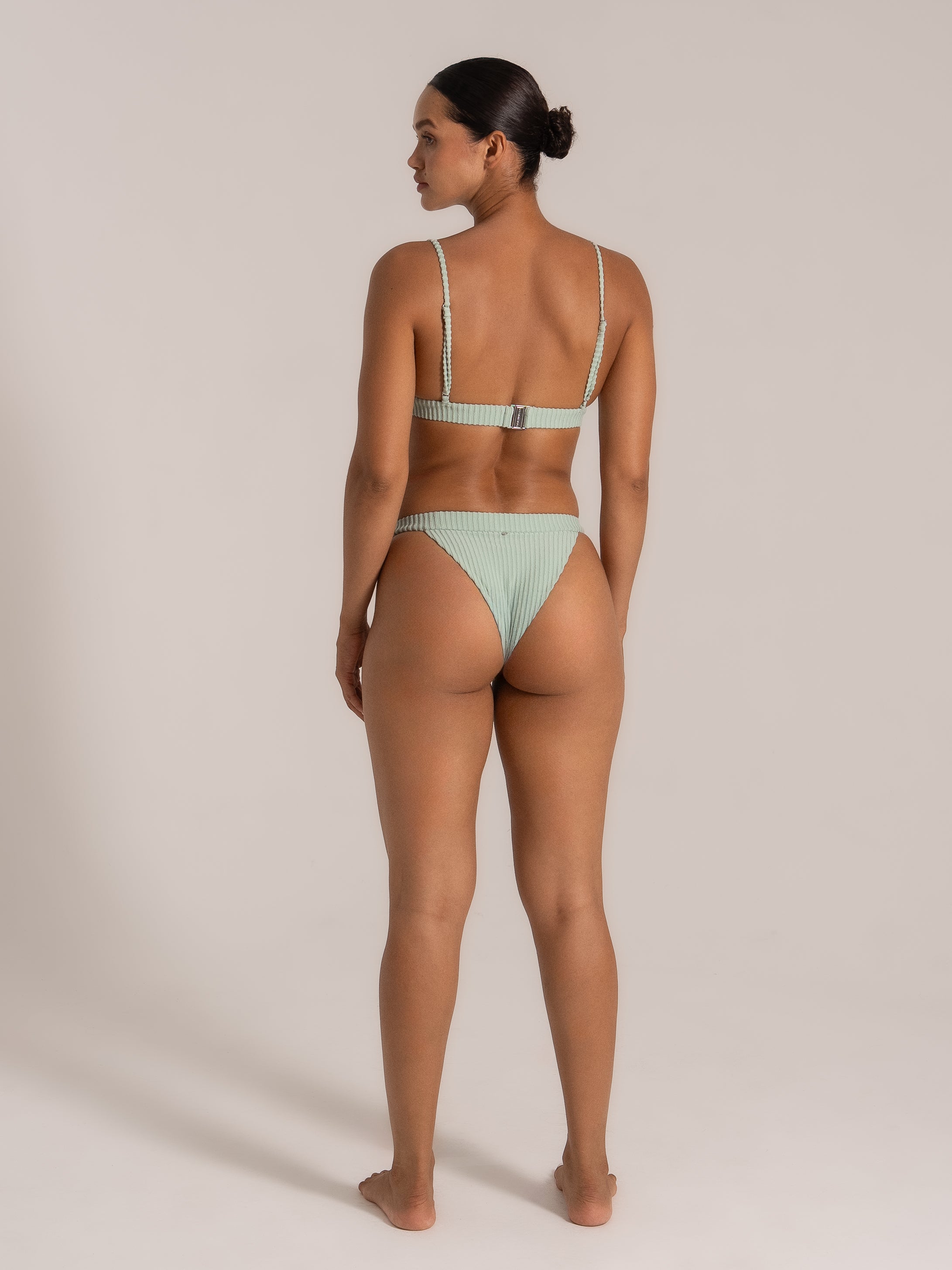 Back view of a model wearing a mint green high-leg bikini with a textured ribbed finish.