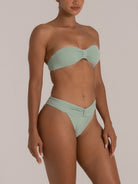 Side angle view of a woman in a mint green strapless bikini with a twist-knot front detail and ribbed texture.