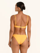 Woman posing in mustard yellow bikini bottom with ruched detail and seamless finish.