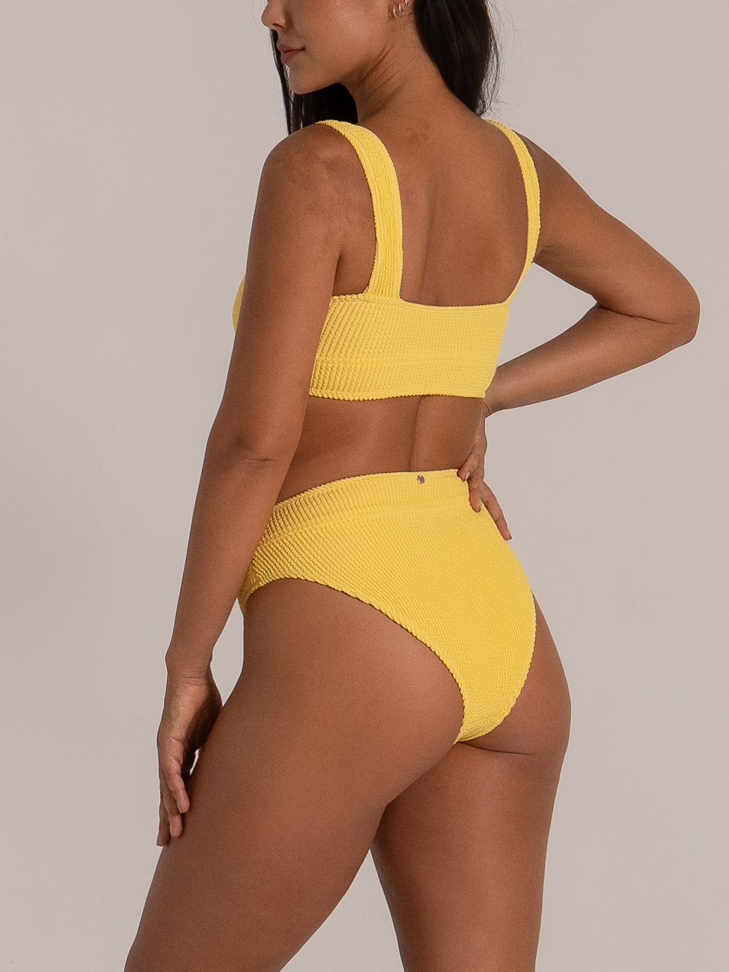 Side-back angle showing mustard yellow bikini bottom in textured stretch fabric