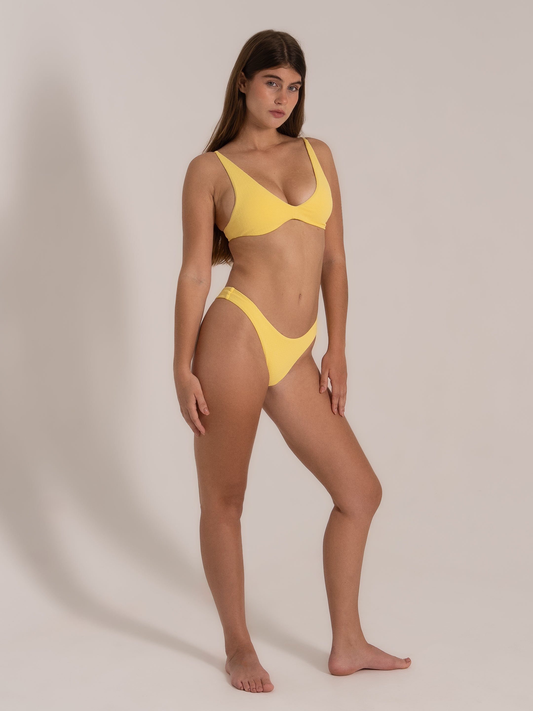 Model in a mustard yellow bikini set with deep V neckline and underwire support, side pose.