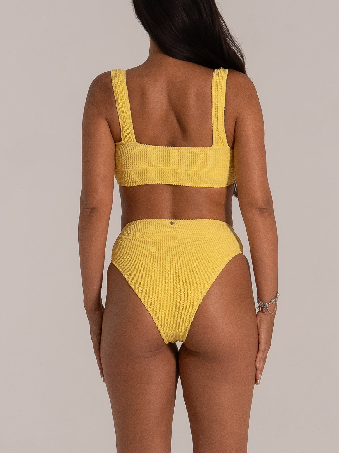 Back view of high-waisted cheeky bikini bottom in mustard yellow textured fabric