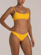 Woman wearing a mustard yellow bikini with textured fabric and thin shoulder straps, front view.