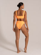Side-back angle of a model in a neon orange bikini with scoop neck and wide straps.