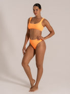 Female model showcasing a bright orange high-leg bikini set from a side-front angle.