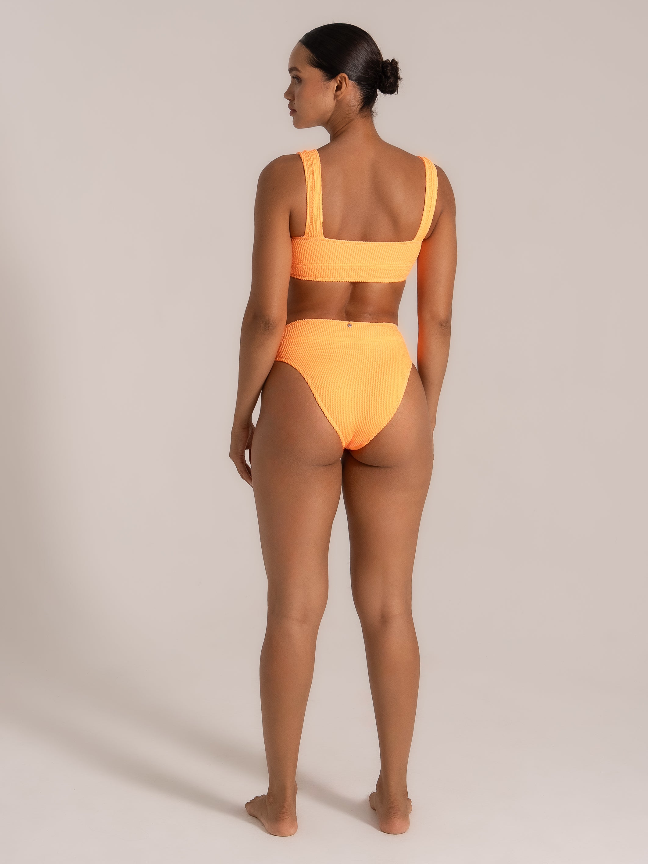 Model wearing a neon orange textured high-waisted bikini set, back view.