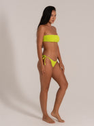 Model showcasing neon yellow bandeau bikini set with ruched side-tie bottoms, angled front view