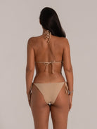 Woman wearing nude triangle bikini set with halter neck and side tie bottoms, back view