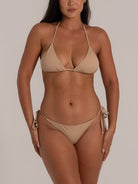 Front view of woman in nude triangle bikini top with adjustable halter ties and matching tie side bottoms