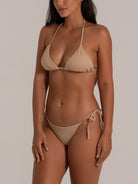 Woman modeling a nude string bikini set with halter triangle top and tie side bottoms, side angle