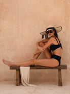OCEAN MYSTERY elegant resort wear: black textured high-waisted bikini set styled with a wide-brim sun hat and red sunglasses.