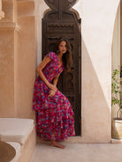 Woman wearing OCEAN MYSTERY tropical floral print maxi dress in pink and purple with tiered skirt.