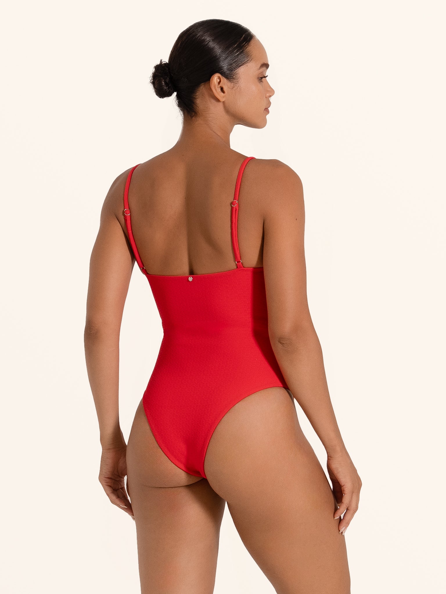 Back angle of woman in red one piece swimsuit with scoop back and cheeky fit.
