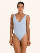 Front view of woman wearing baby blue textured one piece swimsuit with deep V neckline.