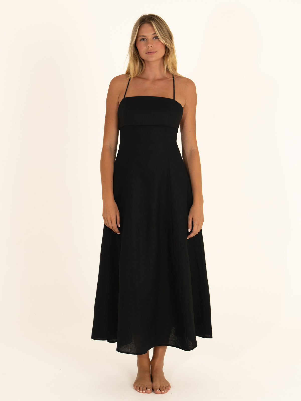Front view of a woman wearing the Ocean Mystery Onyx pure linen midi dress, showcasing the minimalist straight neckline and flowy silhouette.