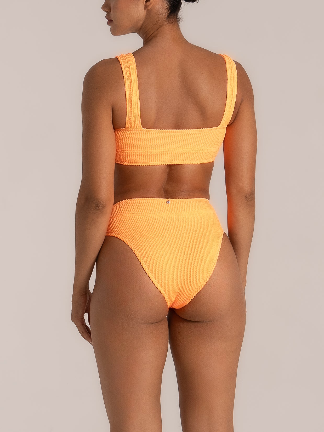 Back view of model wearing orange high waist bikini bottom with textured fabric