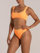 Side angle of a woman modeling a textured orange bikini with scoop neckline and supportive wide straps.