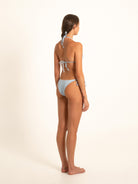Model glancing over shoulder in light blue string bikini, partial back view