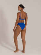 Model wearing royal blue ribbed bikini set with adjustable straps and high waist bottom, back view.