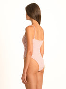 Rear angled view of the peachy pink gingham shirred one-piece, showcasing the tactile texture and high cut leg with seamless-feel edges.