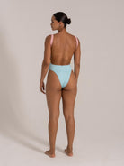 Back view of woman wearing a pink and blue cutout one-piece swimsuit with wide textured straps