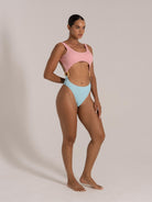 Side view of woman in a pink and blue cutout one-piece swimsuit with ring detail at hips
