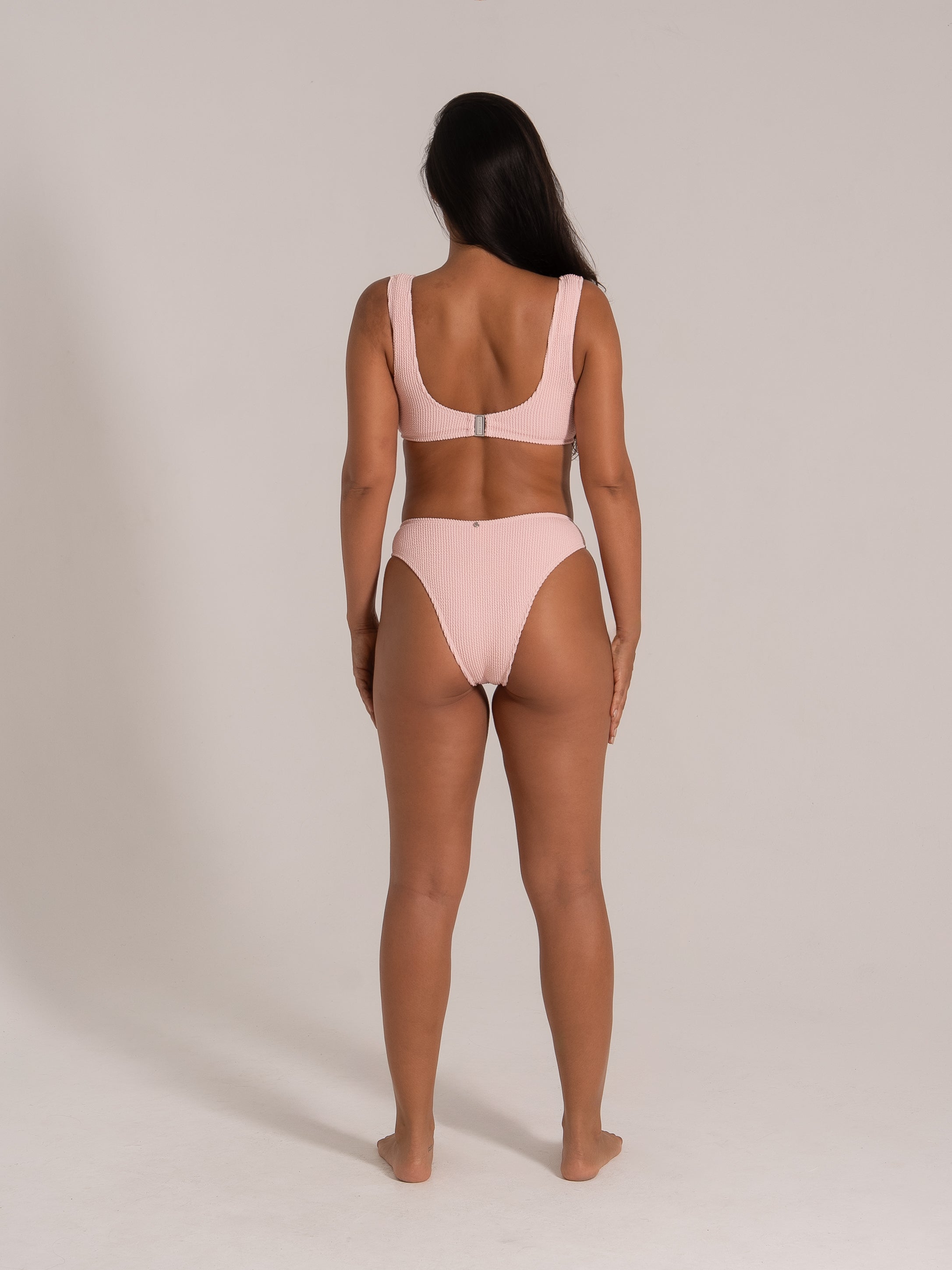 Back view of a model wearing a pink textured bikini set with wide straps and clasp closure.