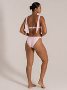 Model showing angled back view of a pink textured bikini set with statement tie straps.