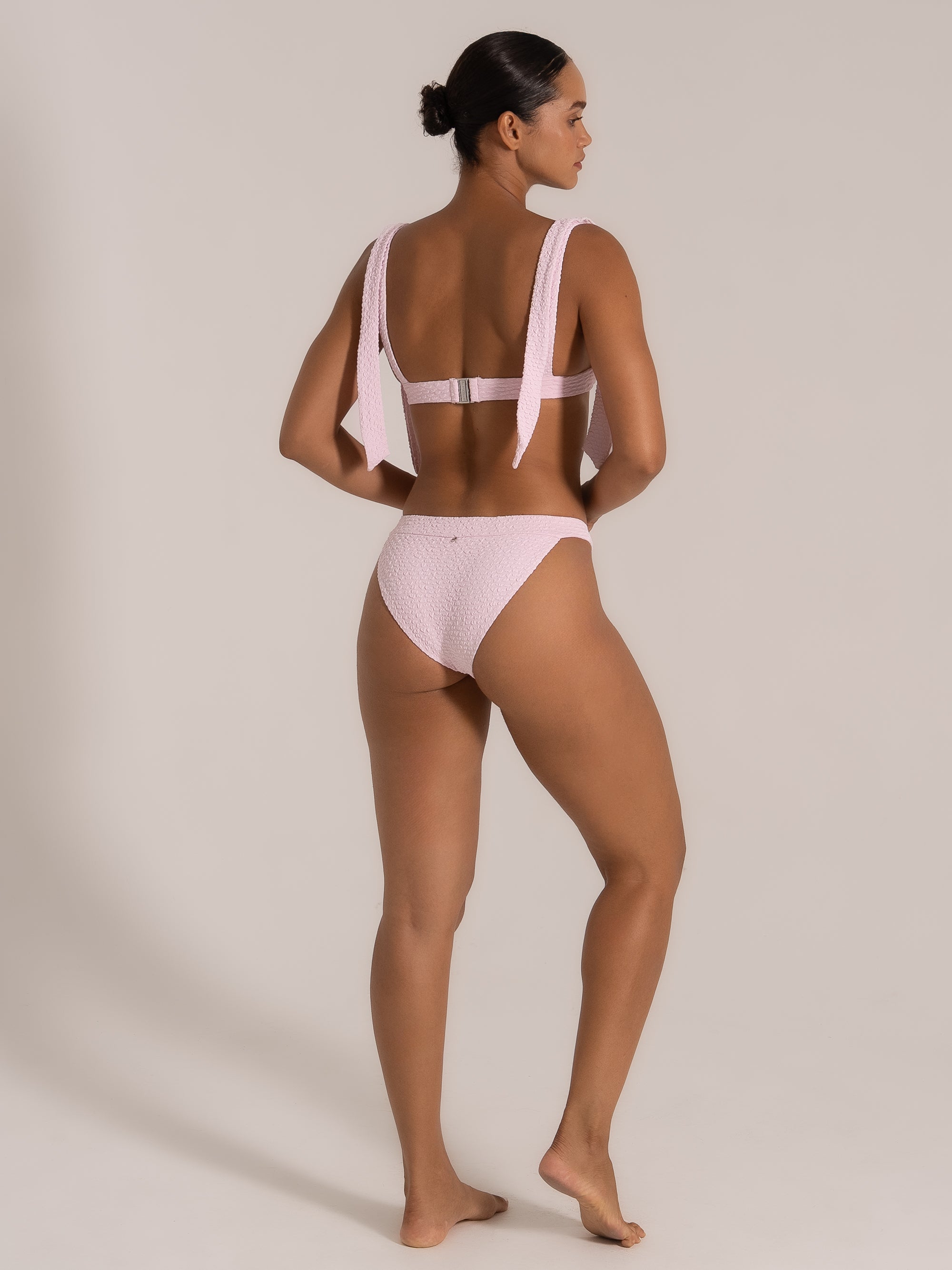 Model showing angled back view of a pink textured bikini set with statement tie straps.