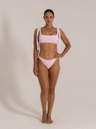 Full front view model wearing a soft pink textured bikini featuring wide tied straps and high-cut bikini bottom.