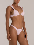 Side view of woman modeling a pale pink textured bikini with thick straps and a gold center detail on the top.