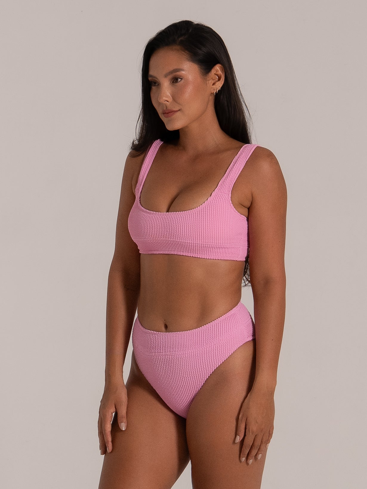 Side pose of model wearing pink textured scoop bikini top with supportive fit