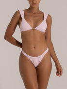 Woman wearing a light pink textured bikini set with thick shoulder straps and a gold trim at the center of the top.