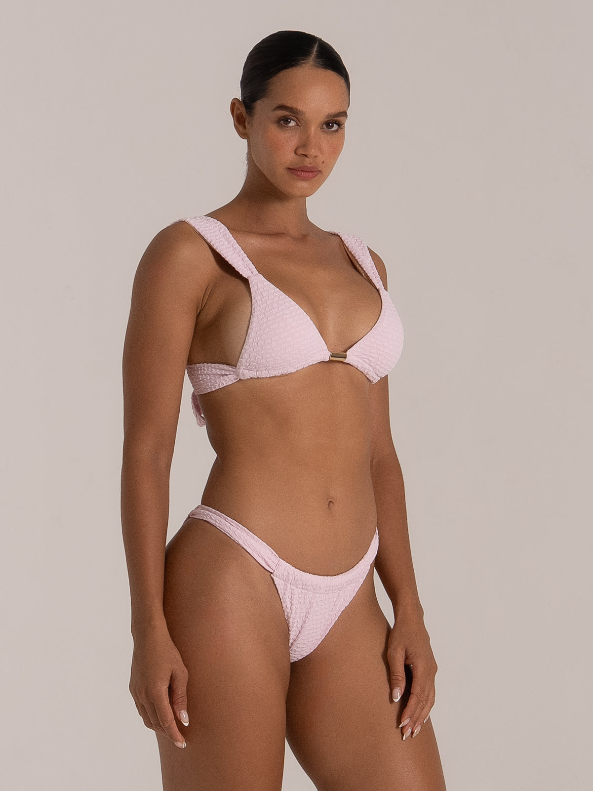 Side angle of pink triangle bikini top with textured stretch fabric and gold bar detail