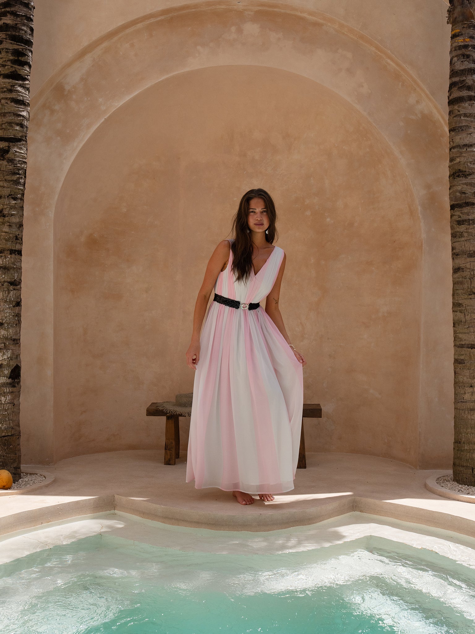 Lifestyle photo of pink V neck maxi dress with black belt worn poolside