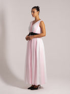 Elegant side view of a sleeveless pink and white maxi dress with a black waistband, styled with black heels.