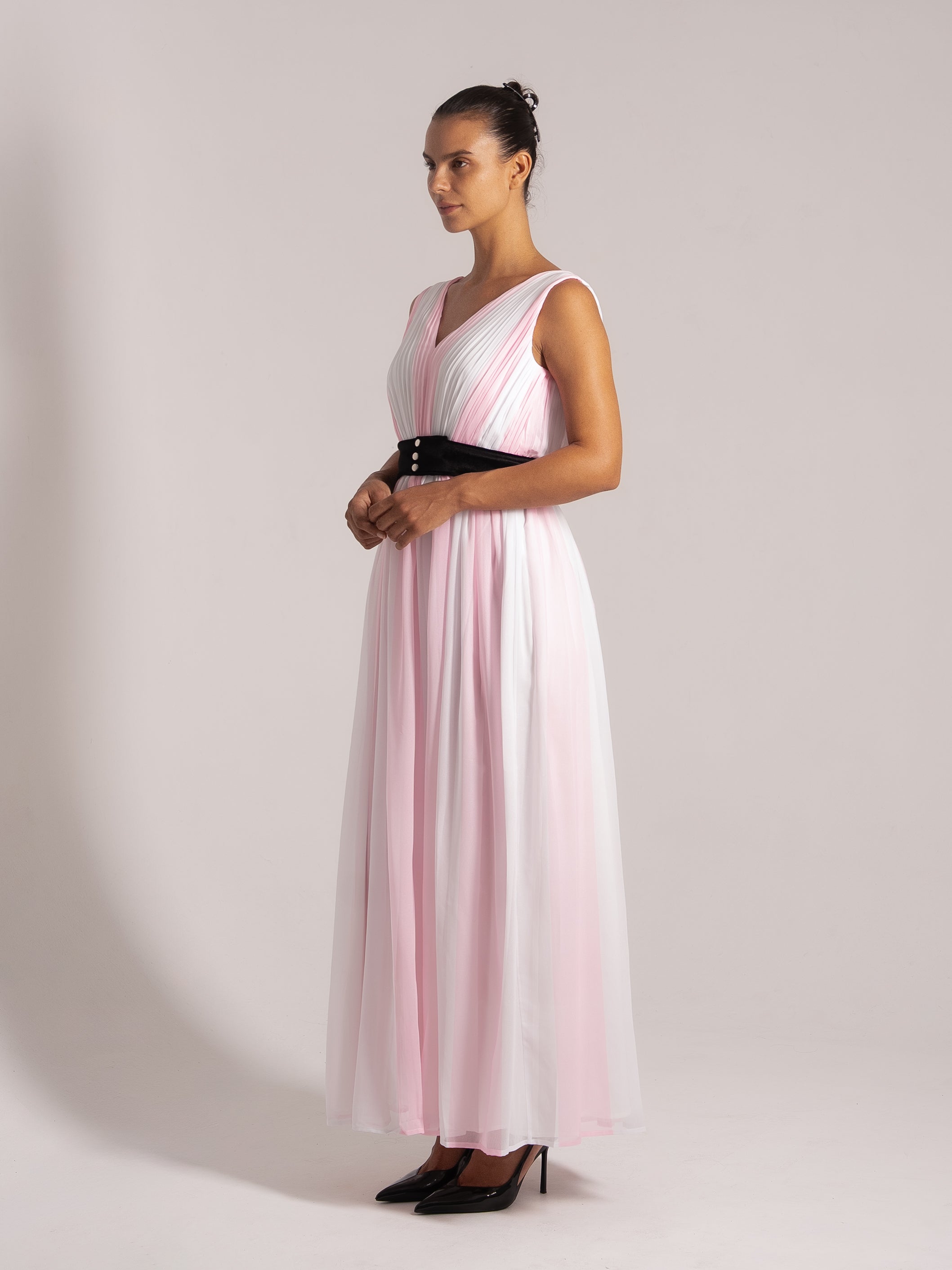 Elegant side view of a sleeveless pink and white maxi dress with a black waistband, styled with black heels.