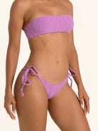 Side angle of purple tie side bikini bottom with adjustable ties and minimal coverage.
