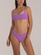 Woman in a stylish purple bikini with textured fabric and scoop neckline, front angle pose.