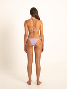 Model from behind wearing violet halter bikini with flattering cheeky cut and clean background