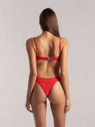 Rear angled view of woman wearing red textured bikini with adjustable straps.