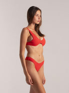 Woman in red bikini with thick straps and sculpted underwire front, side view.