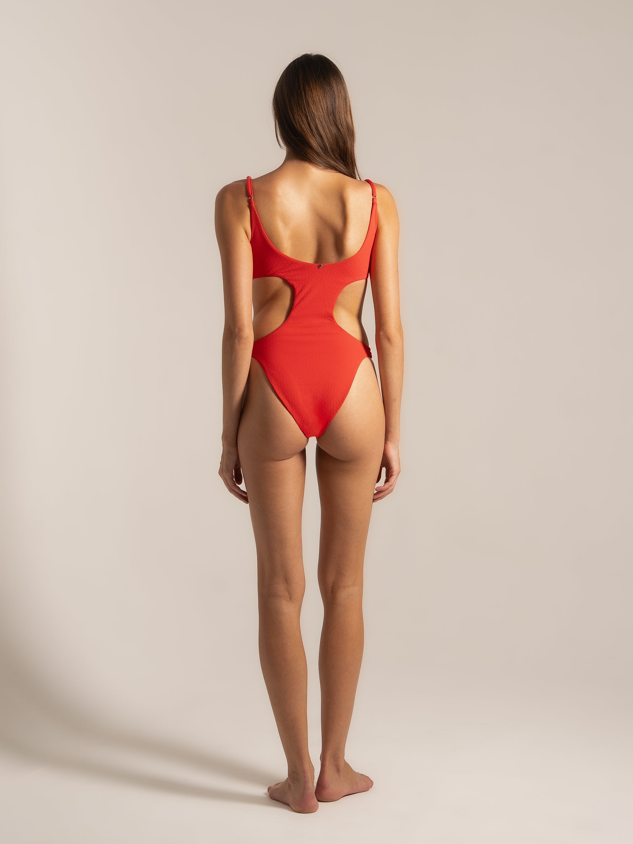 Back angle of red cut-out one piece swimwear featuring high-cut legs and textured fabric