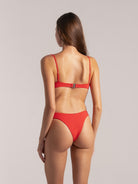 Woman in red textured bikini showing back clasp and high-cut bottom.
